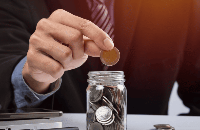 Close-up of a person saving coins in a clear jar to illustrate calculating returns on localized marketing investments.