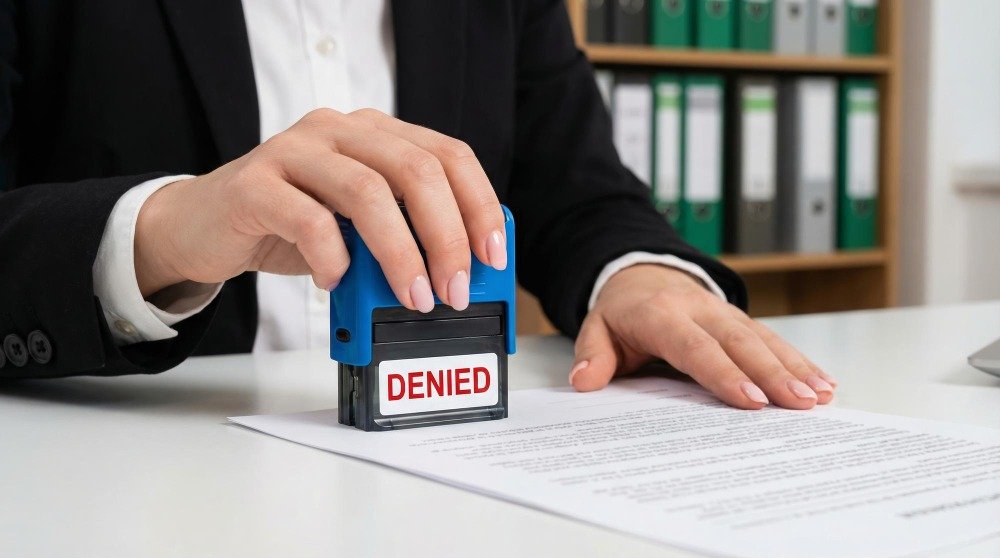 A hand stamping a red "DENIED" seal on an official document, illustrating the costly consequences of legal translation errors.