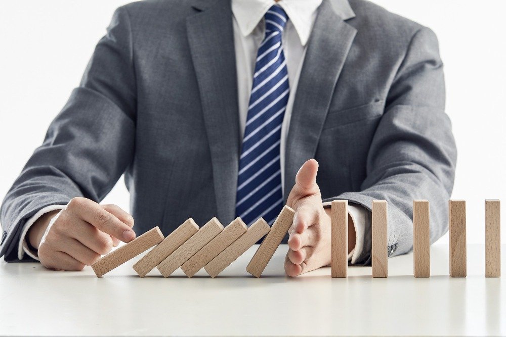 A businessman using his hand to stop a line of falling wooden dominoes, illustrating risk mitigation and legal translation strategy safeguards.