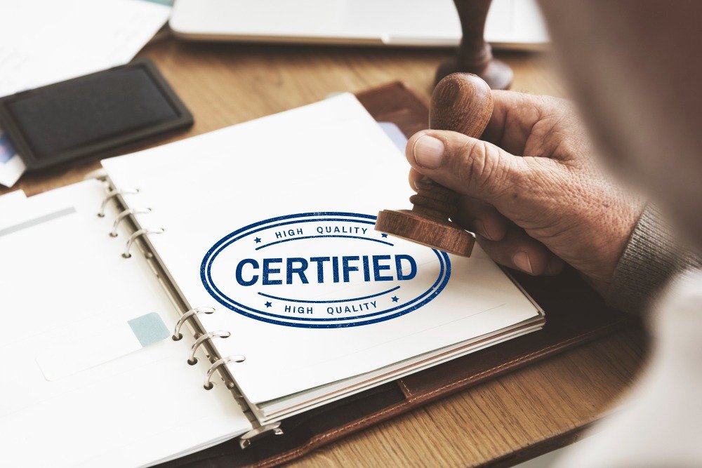 A hand stamping a blue "HIGH QUALITY CERTIFIED" seal onto an official binder document, representing certified translation for B2B contracts.