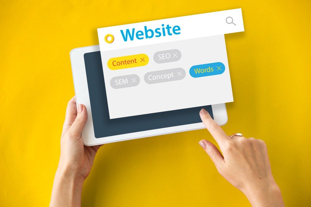 Hands holding a tablet displaying a search interface with digital marketing tags like SEO, Content, and Words against a yellow background, representing strategic localized SEO.