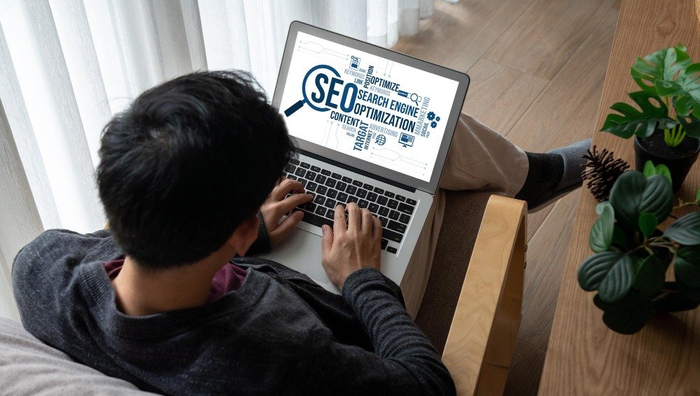 A person relaxing on a chair while working on a laptop displaying SEO word cloud graphics, representing multilingual SEO integration into content workflows.