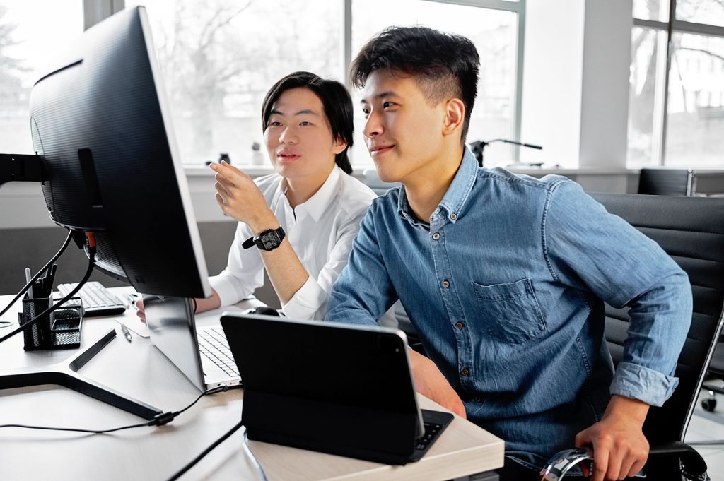 Two colleagues sitting at a computer desk, pointing to a monitor as they evaluate vendor performance data.